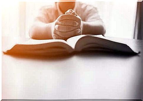 Child with folded hands in front of open book