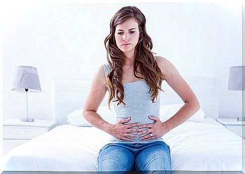 Woman sitting on bed and holding on to her stomach